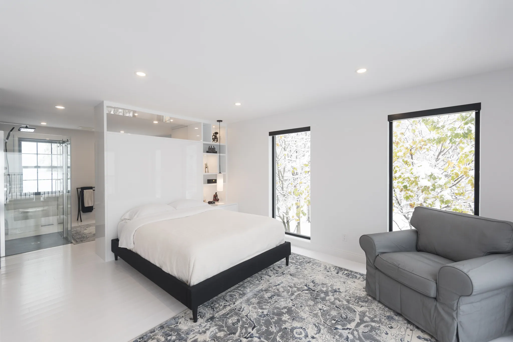 Chambre minimaliste et lumineuse avec lit blanc, grande fenêtre et vue sur la nature enneigée.