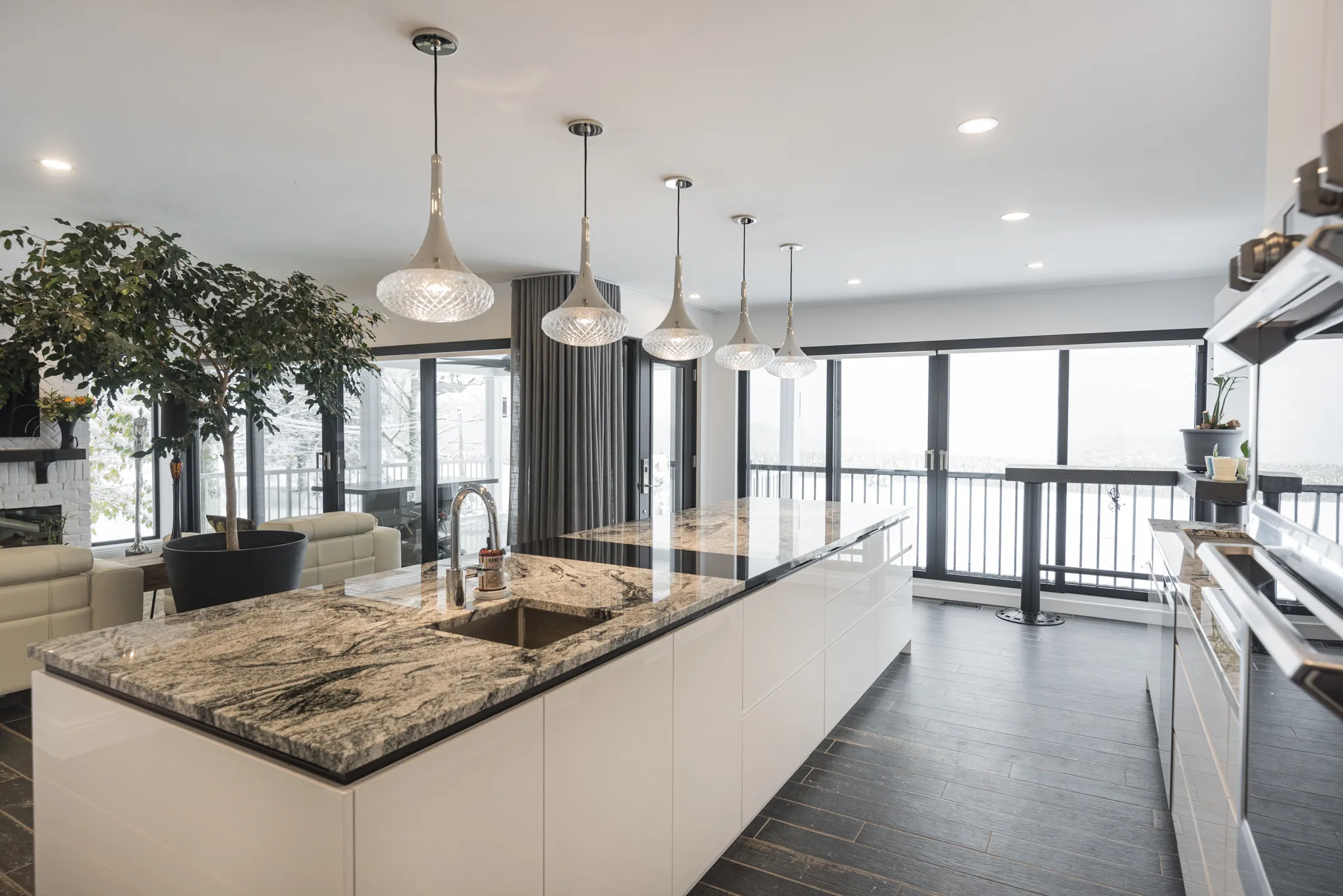 Cuisine design avec îlot central en marbre, luminaires suspendus et vue panoramique.