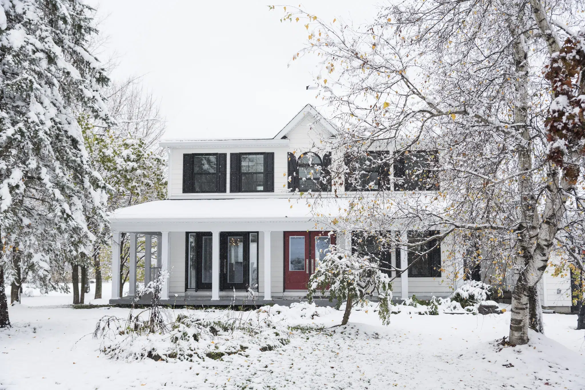 Maison blanche traditionnelle sous la neige avec façade classique et volets noirs.