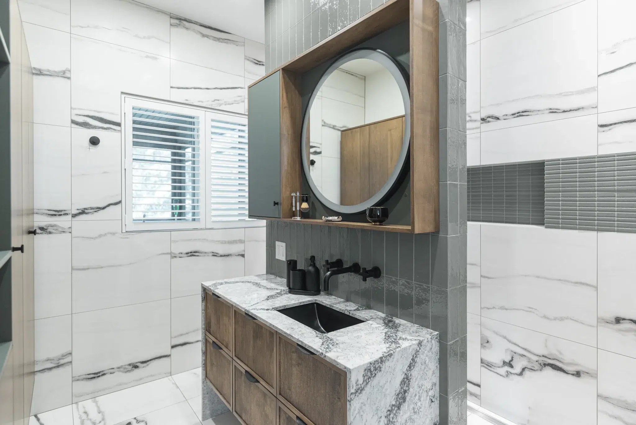Salle de bain élégante avec meuble en bois, plan de travail en marbre et miroir rond encastré.
