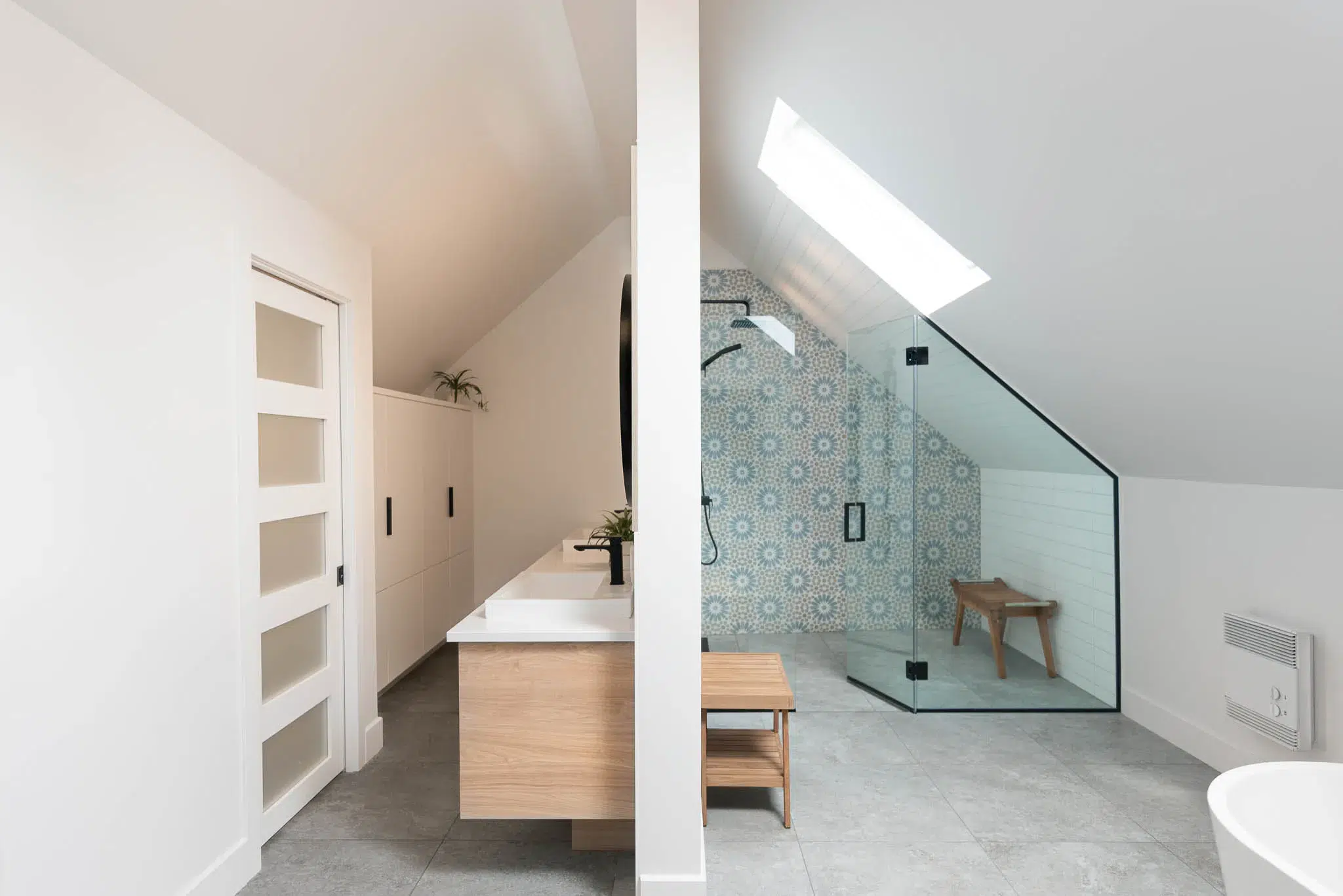 Salle de bain sous combles avec douche en verre et carrelage à motifs bleus.